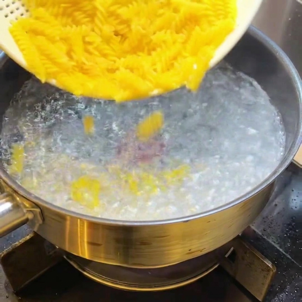 Dry fusilli pasta being dropped into a pot of boiling water.