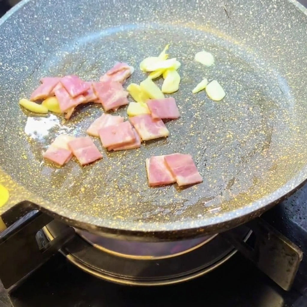 Chopped bacon pieces frying in a pan with garlic.