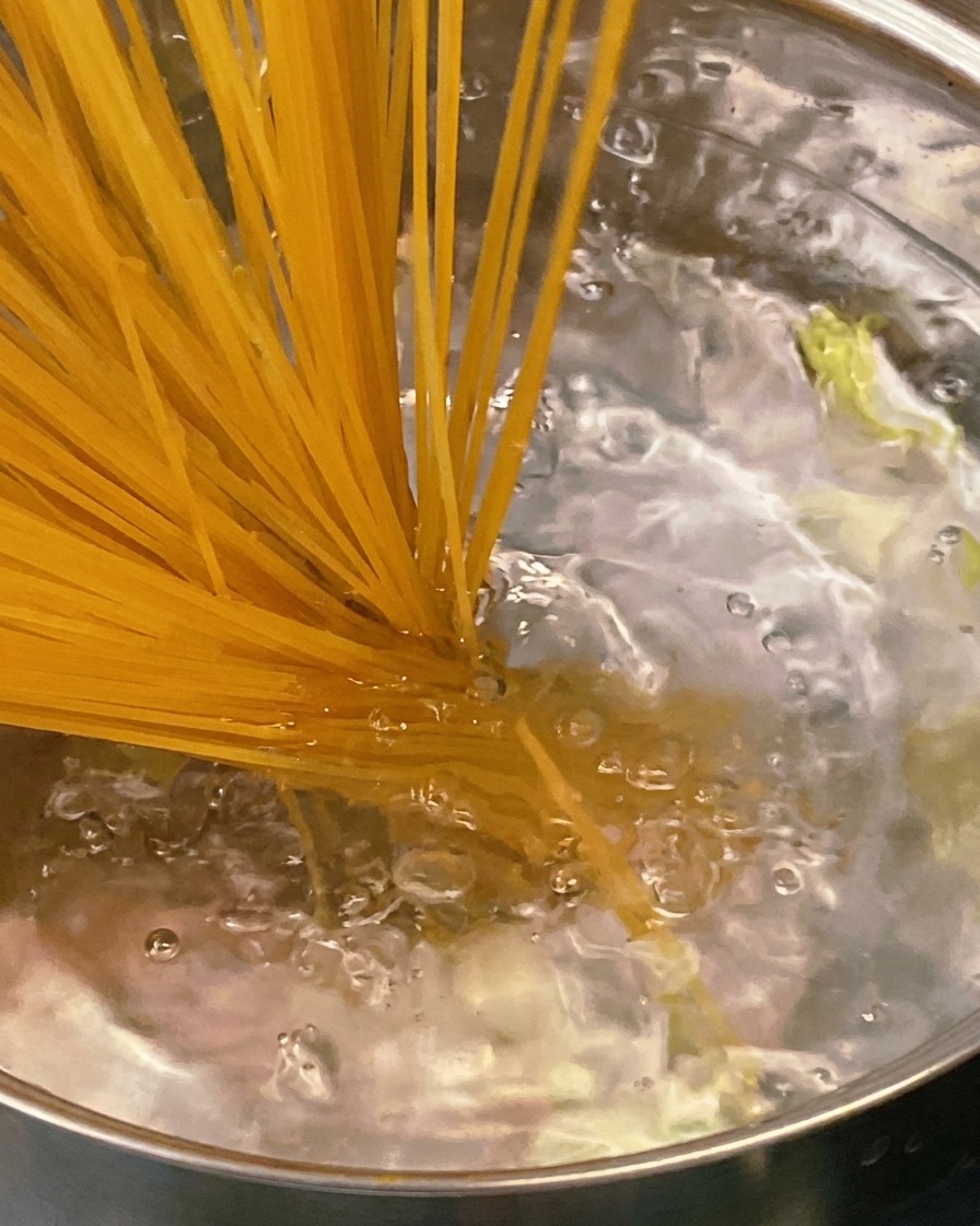 A wooden spoon stirring a thick, savory tomato and bacon sauce in a stainless steel pan.