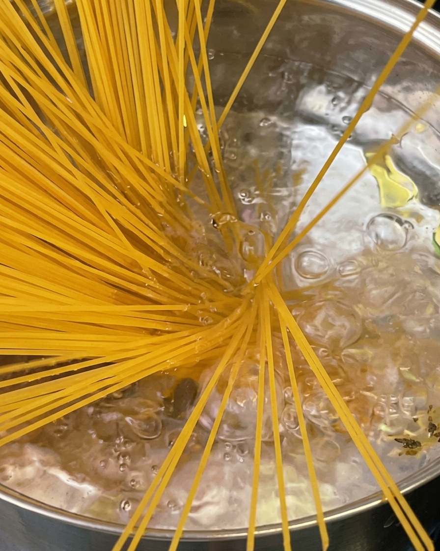 Al dente pasta being lifted from a pot with a serrated pasta fork, steam rising above the pot.
