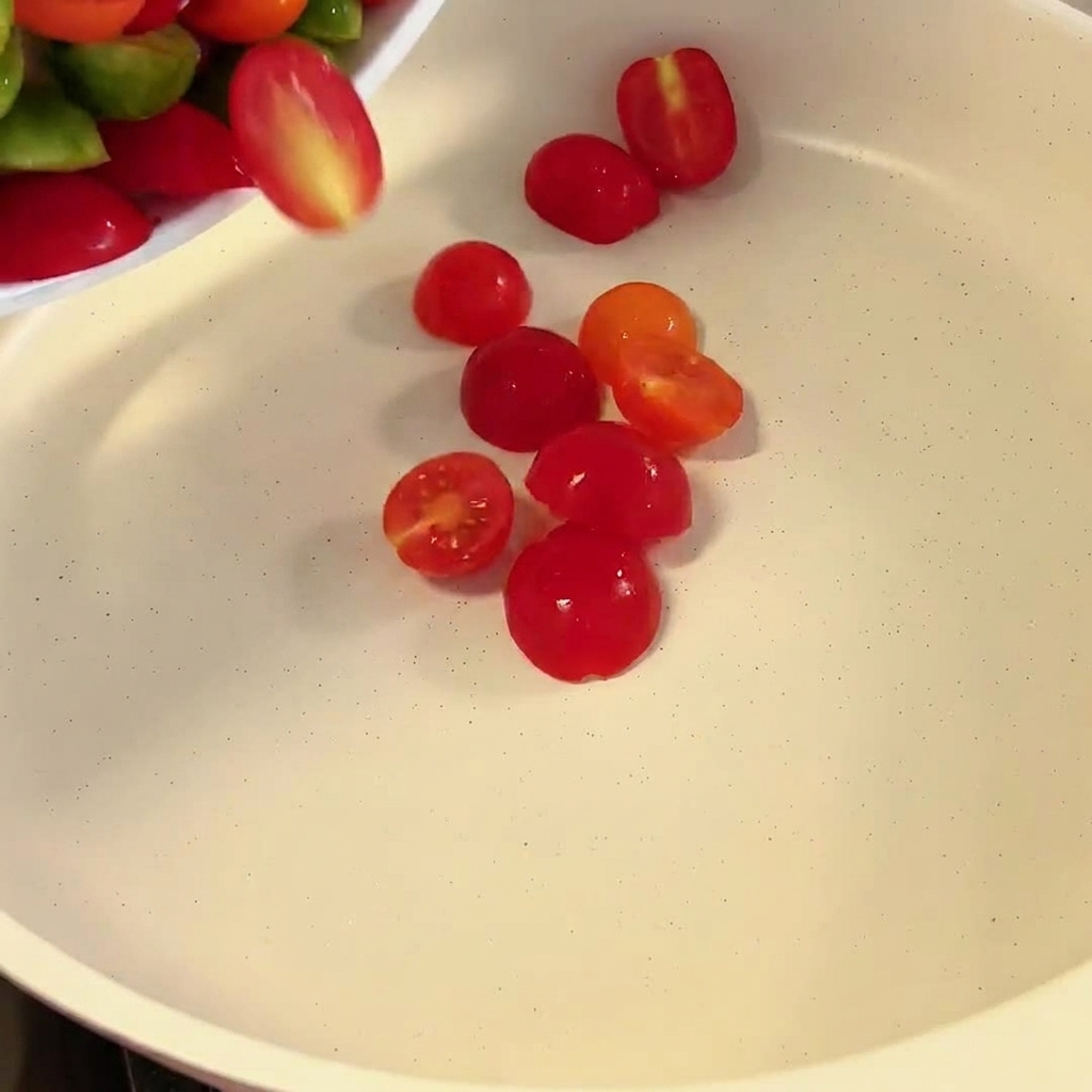 Halved red and green cherry tomatoes falling into a white pan.