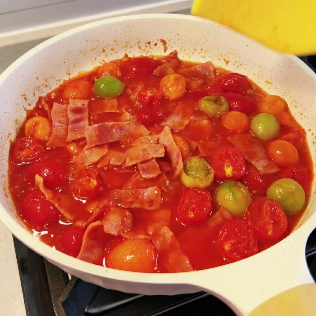 A slice of yellow cheese melting into a simmering tomato and bacon sauce.