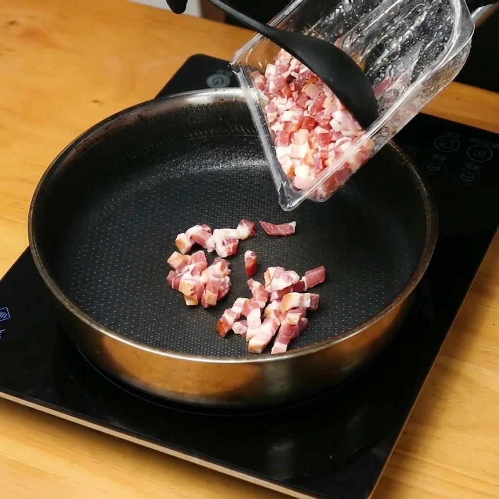 Chopped bacon pieces browning and releasing fat in a hot skillet.
