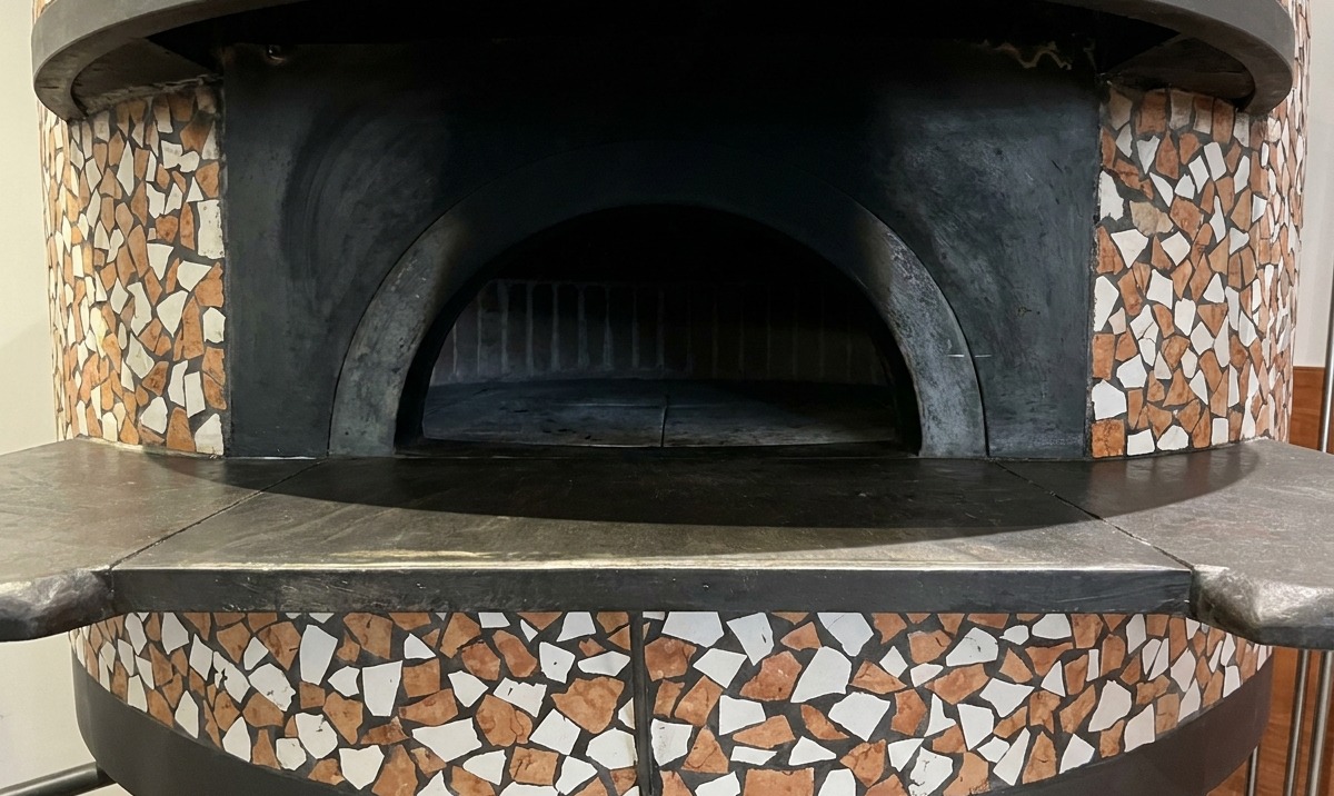 A pizza baking inside a brick oven, with the crust edges bubbling and browning near the flames.