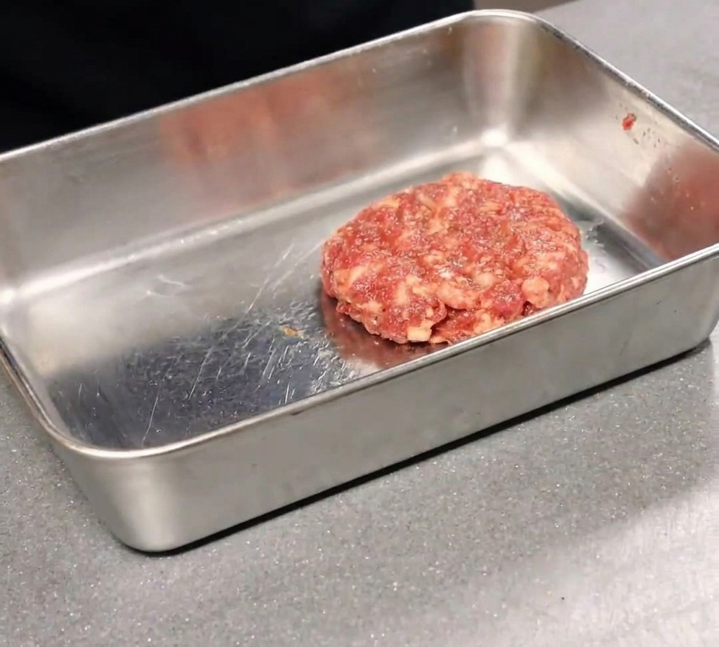 A hot, freshly baked pizza being cut into slices with a rolling pizza wheel on a wooden board.