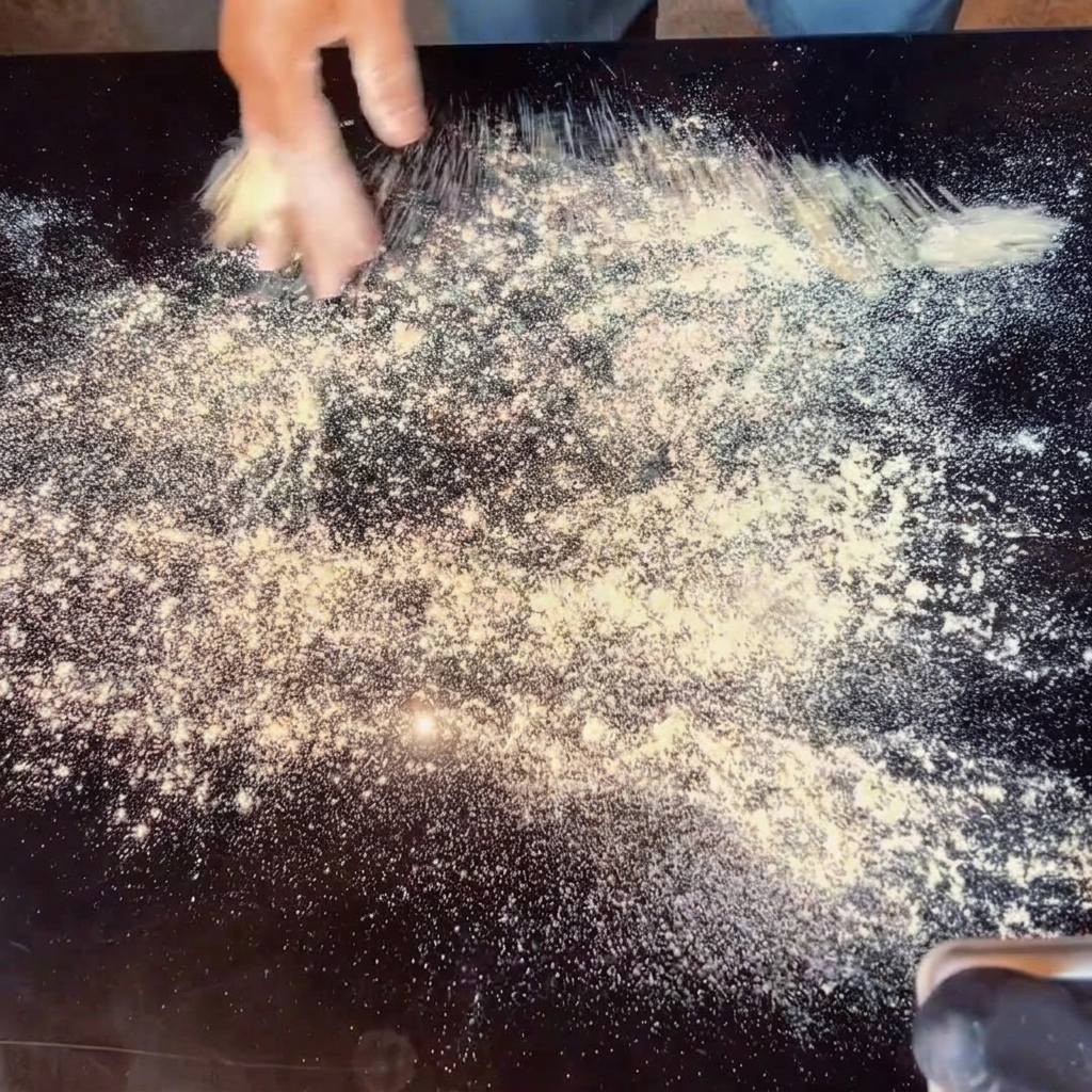 Hands stretching pizza dough on a floured surface.