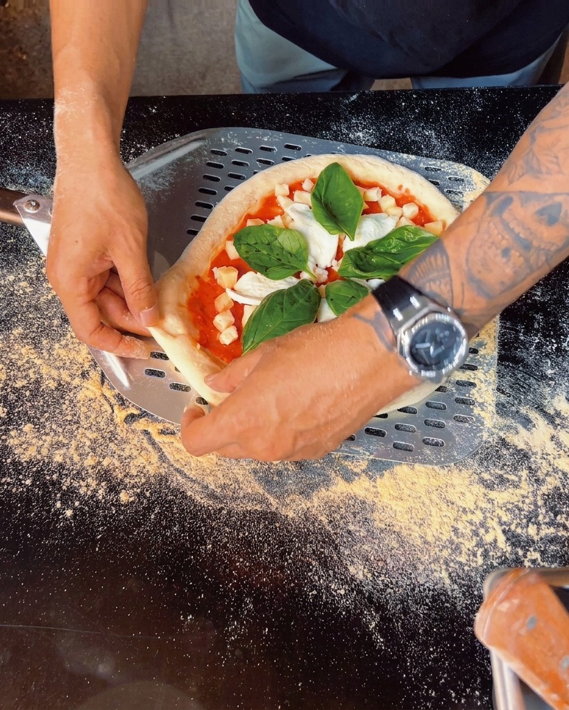 Close up of fresh basil leaves being placed onto the topped pizza.