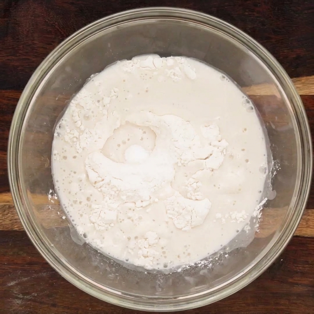 The liquid and dry ingredients combined in a glass bowl, forming a shaggy dough mixture.