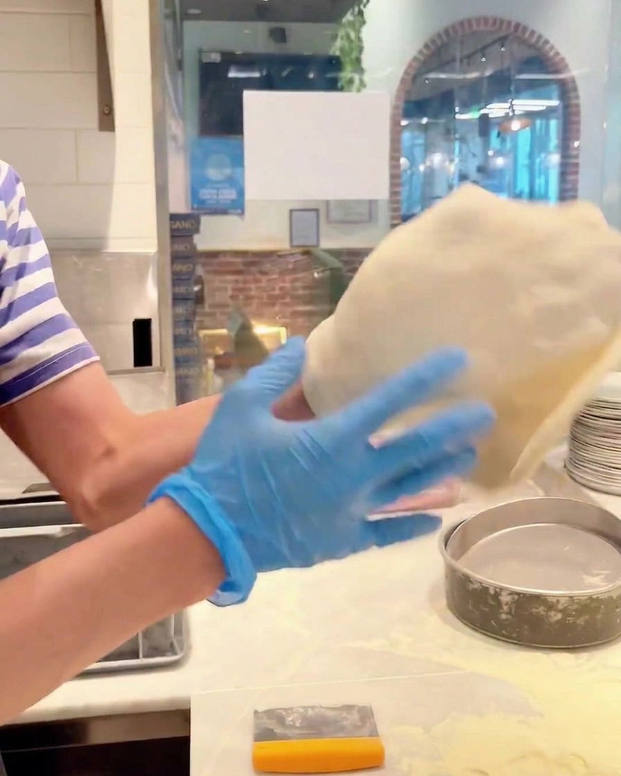 Hands rotating a piece of pizza dough to stretch it into a larger circle.