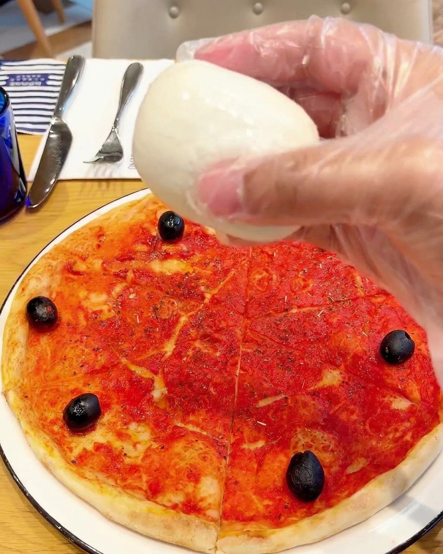 Chunks of fresh buffalo mozzarella being placed onto the pizza.