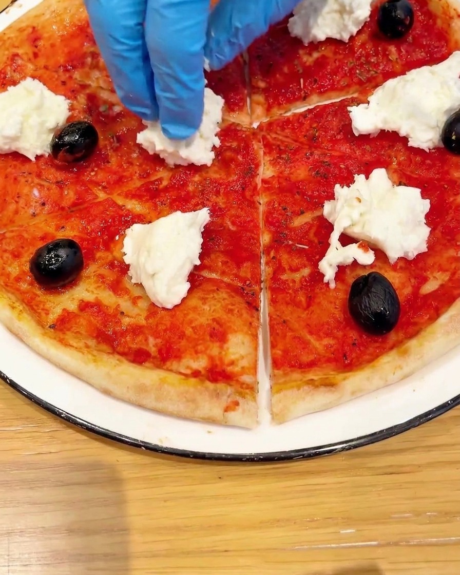 Top-down view of a pizza base being garnished with fresh cherry tomatoes and green basil leaves.