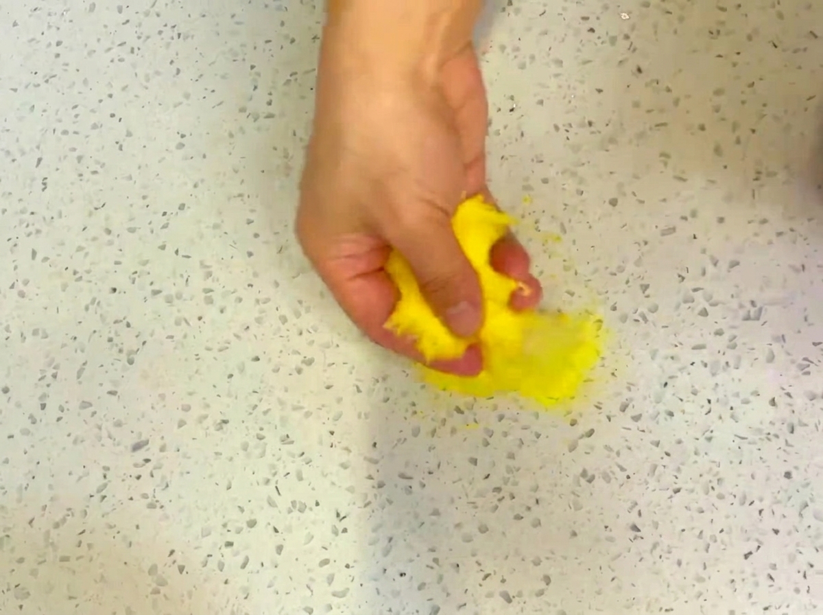 A flat, circular pizza dough being stretched out on a surface lightly dusted with cornmeal.