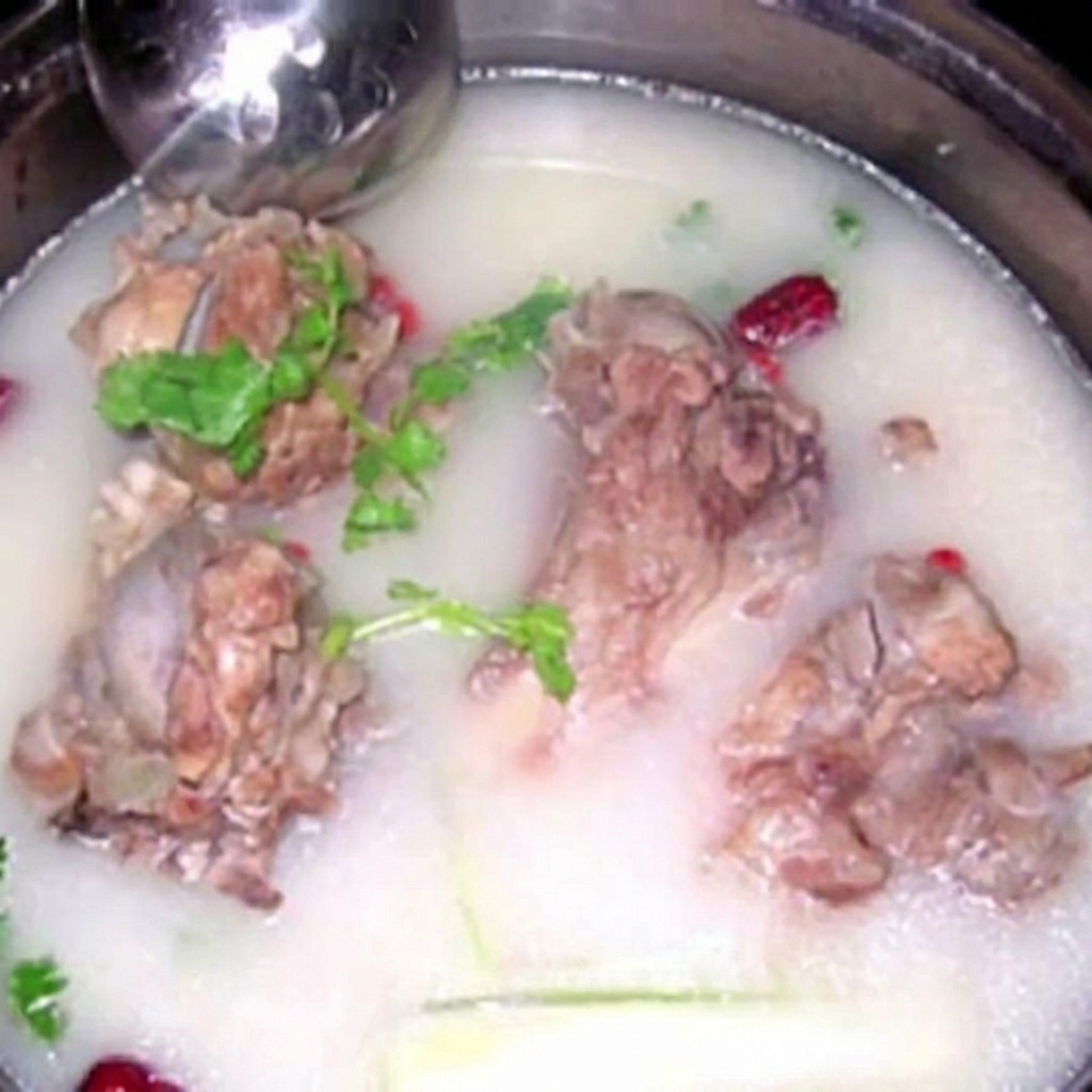 Several large pork bones submerged in a milky, opaque broth, garnished with fresh herbs.