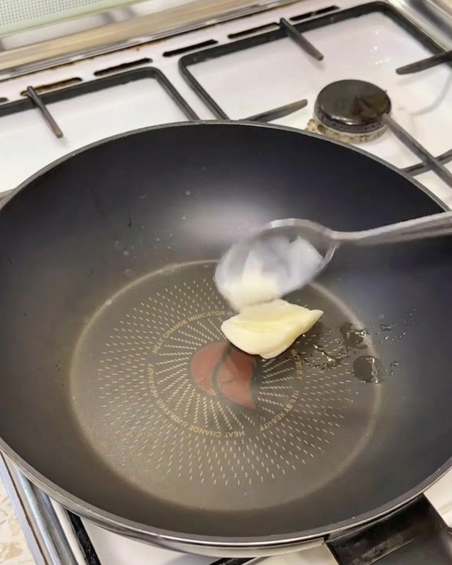 A spoonful of white lard melting in a hot black frying pan.