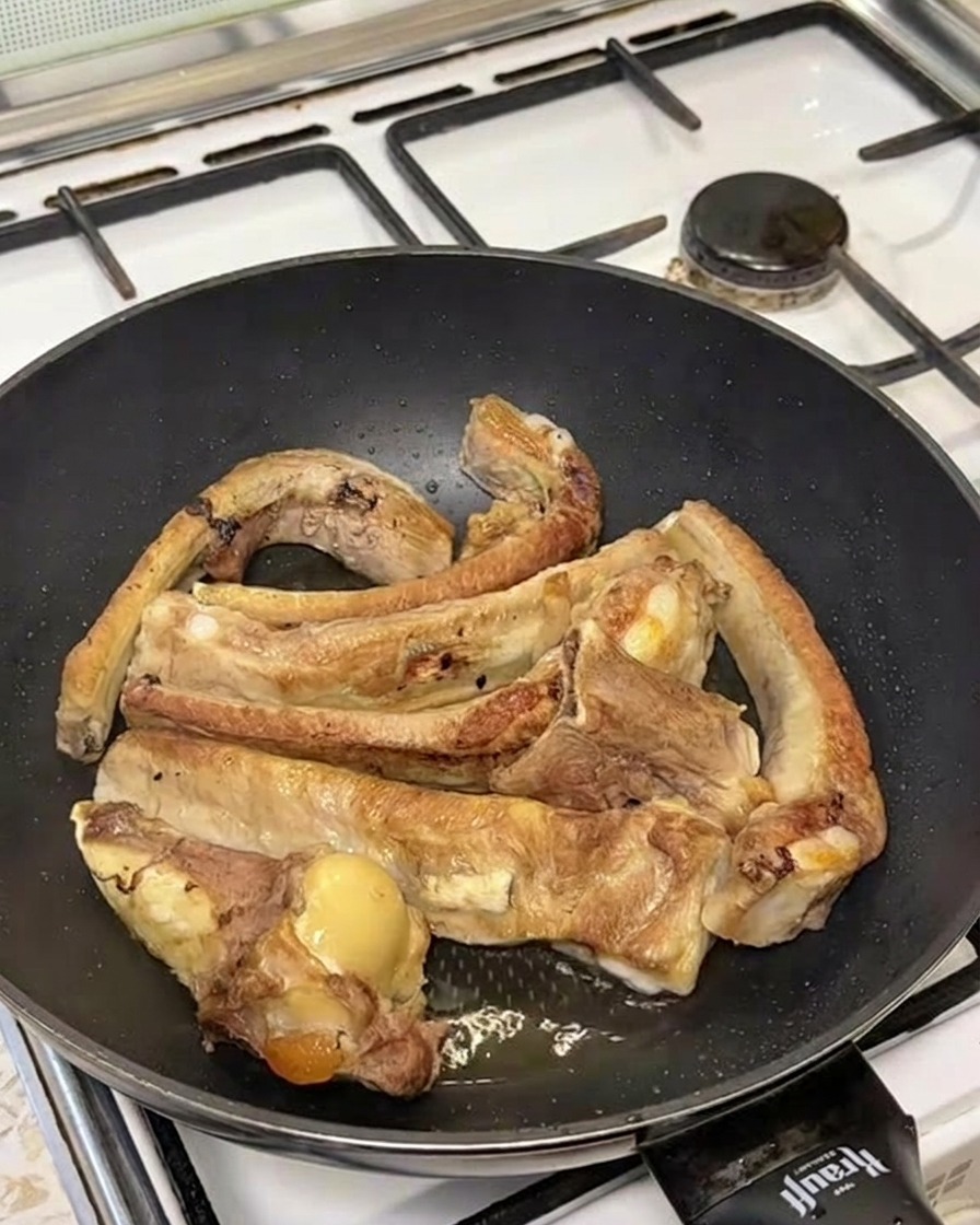 Boiling water being poured over seared ribs in a pan, creating a cloud of steam.