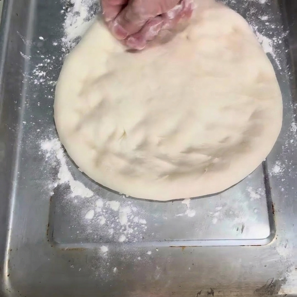 The dough being flattened into a round shape on a baking sheet.