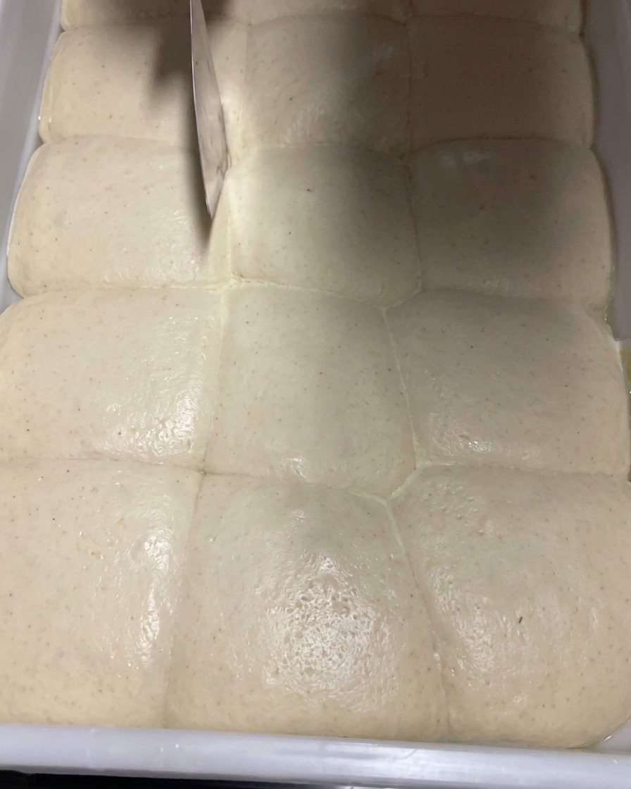 A close-up of fermented dough being carefully divided into portions using a metal dough cutter.