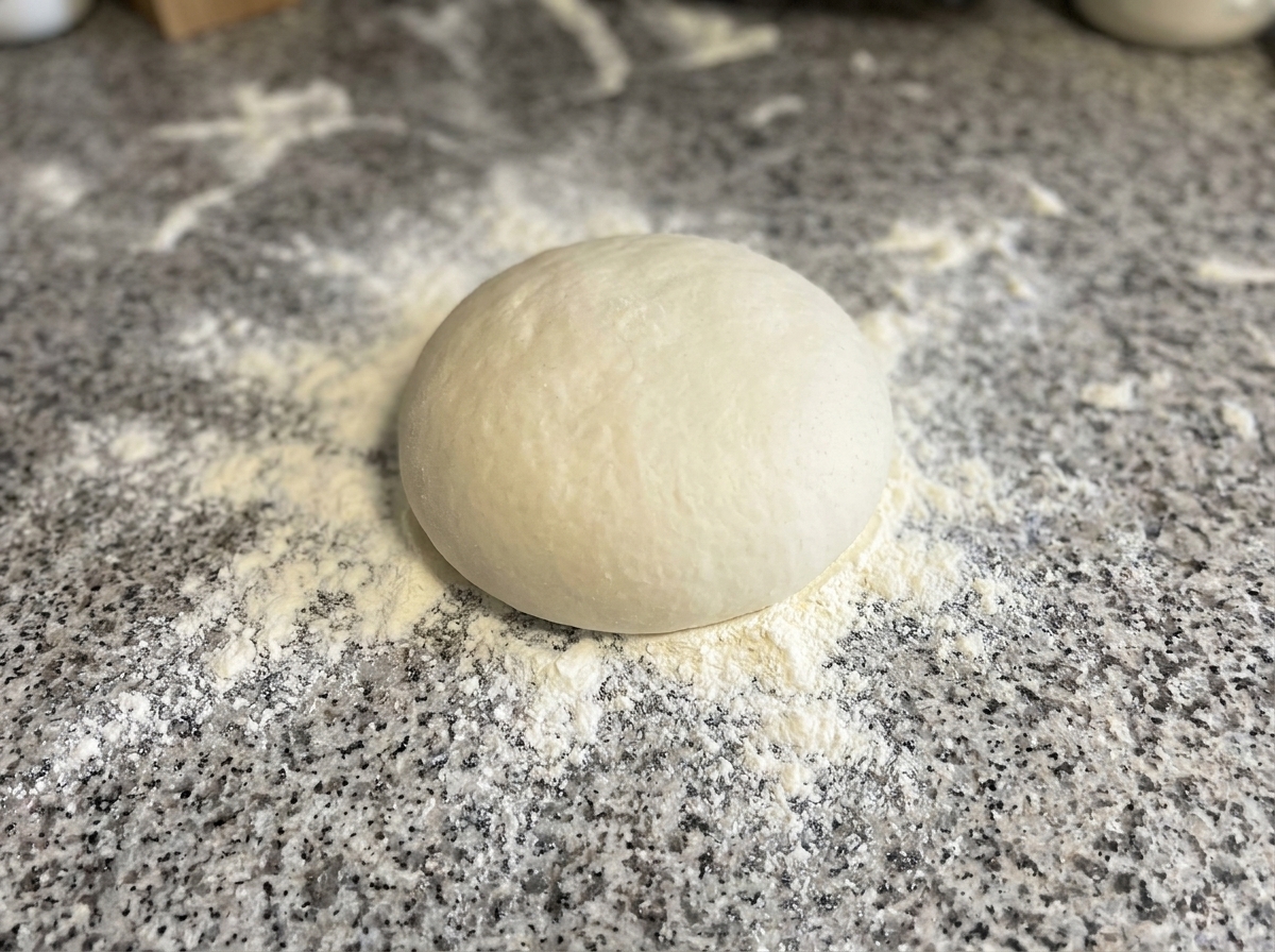 Dough being pressed and shaped into a circle on a floured surface.