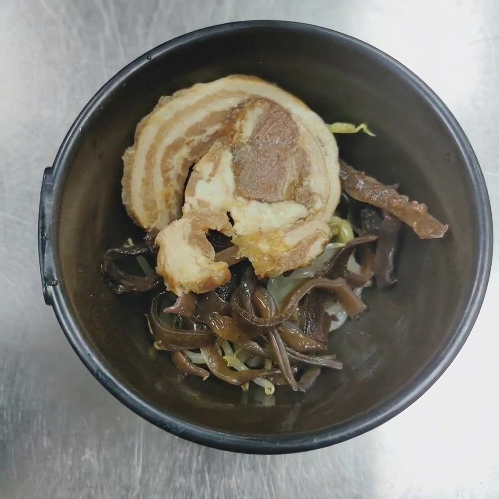 A close-up of a serving bowl containing rolled chashu pork and wood ear mushrooms ready for plating.