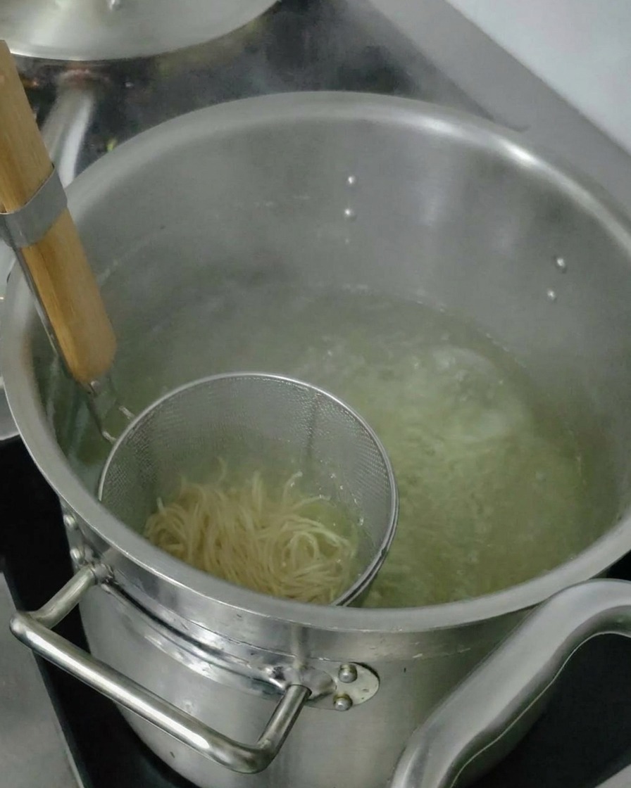 Cooked ramen noodles being lifted in a strainer to drain excess water before adding to the bowl.