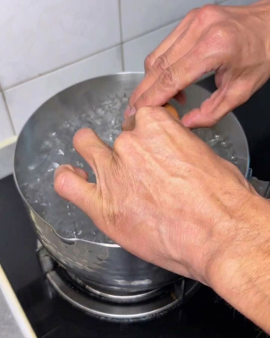A raw egg being cracked into a pot of boiling water.