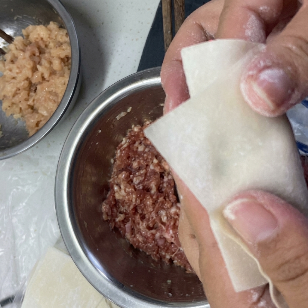 Hands folding a wonton wrapper around the filling and sealing the edges with water.