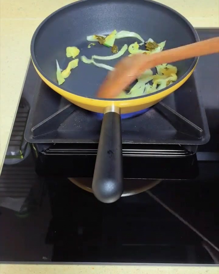 Pickled mustard greens being sautéed in a yellow pan with a wooden spatula.