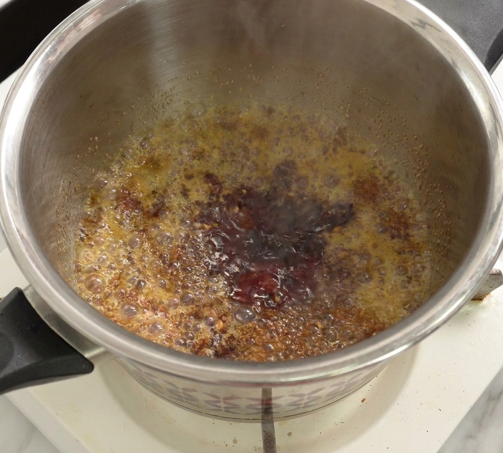 A mixture of tomato sauce and vinegar simmering and bubbling in a pot on a stove.