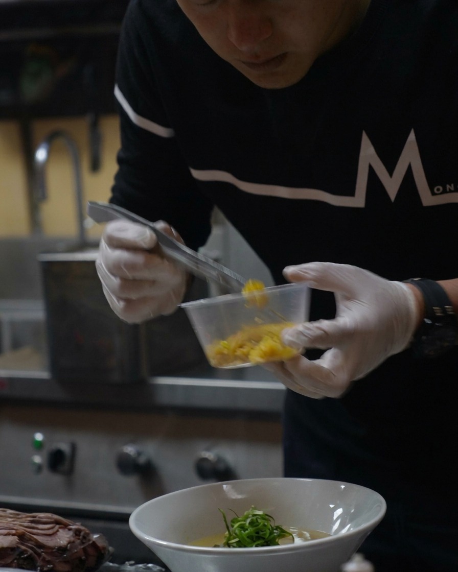A small spoonful of bright yellow yuzu zest being sprinkled over the finished ramen.