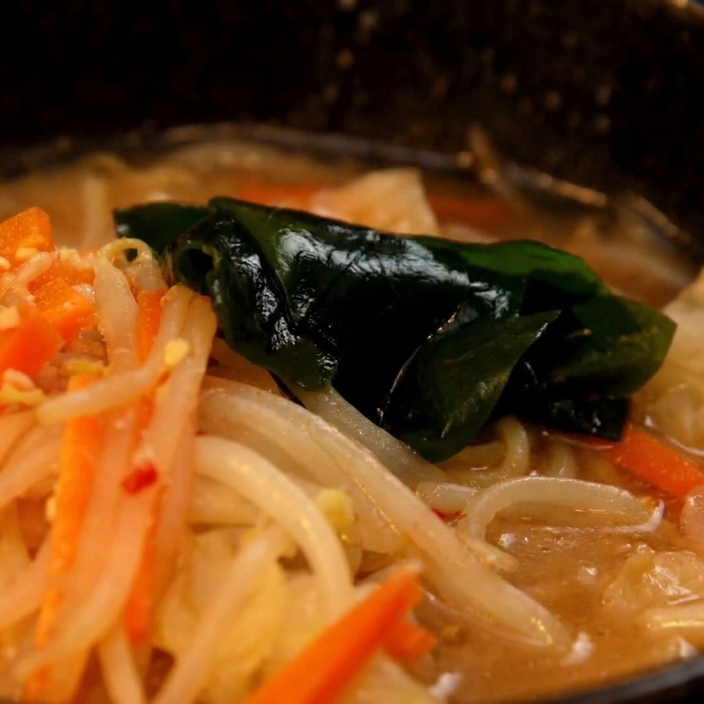 Cooked ramen noodles being moved from a pot into the prepared miso soup base bowl.