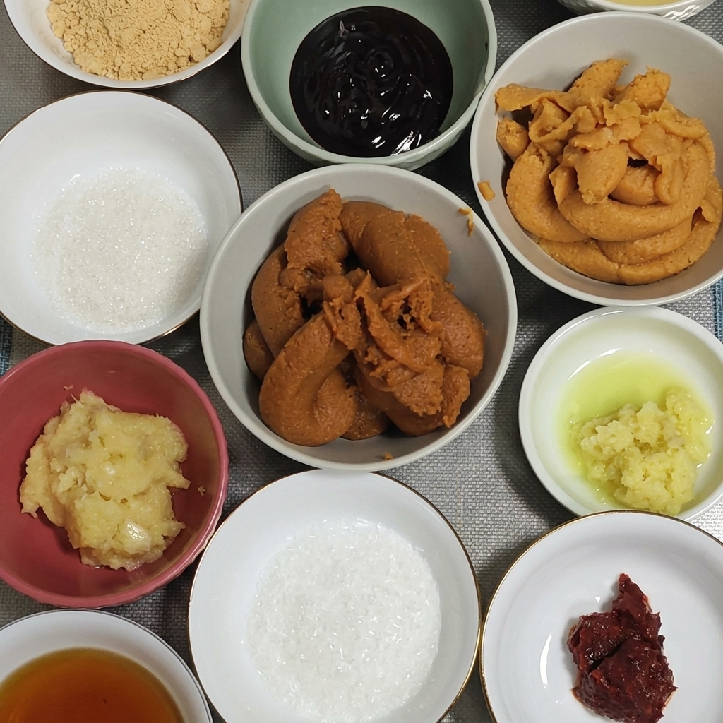 A large spoonful of thick, dark red miso paste being lowered into a bowl with garlic and ginger.