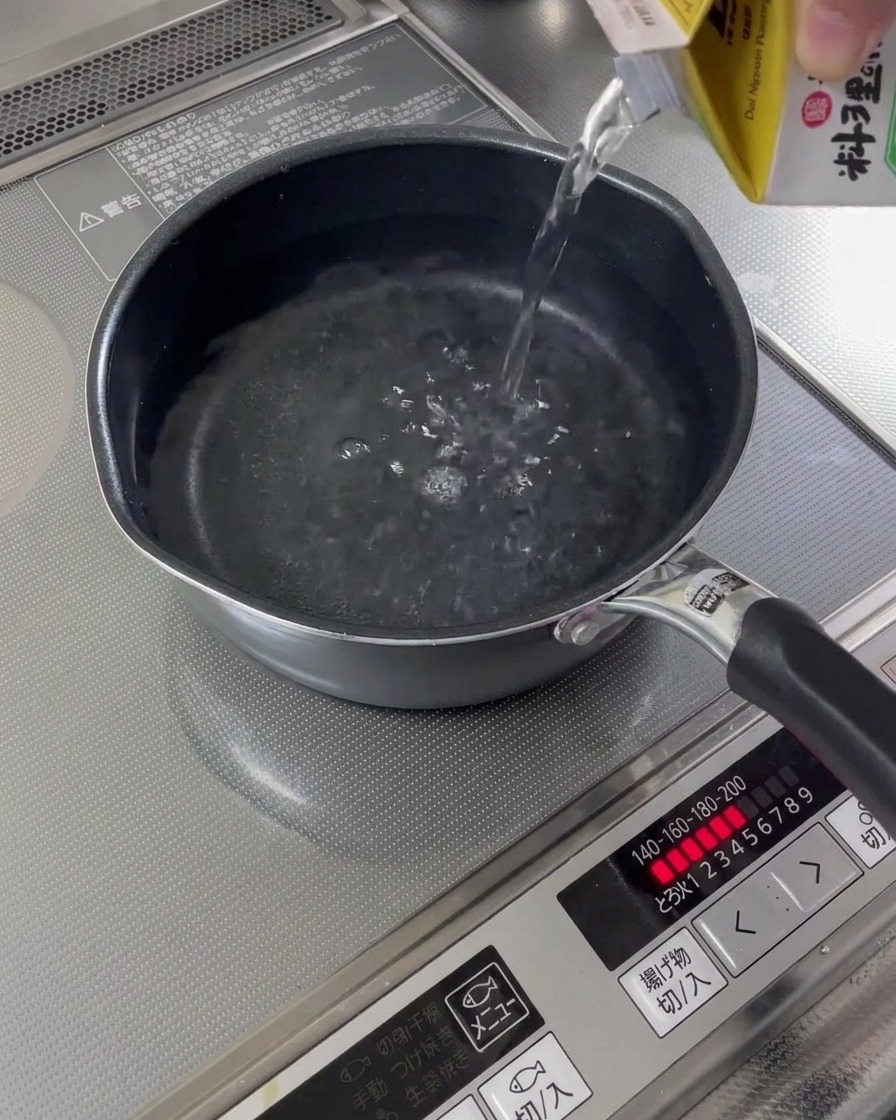 Water being poured from a carton into a small saucepan on the stove.