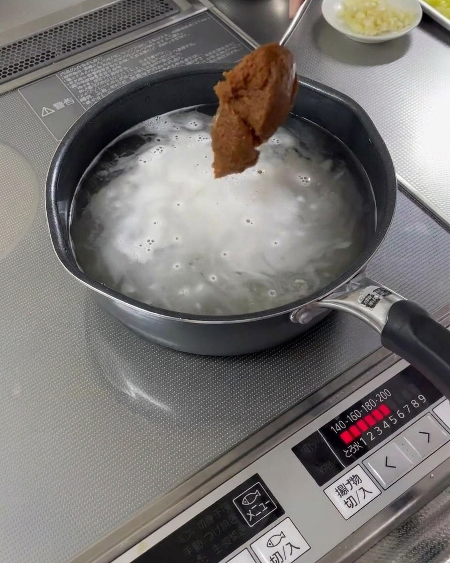 A spoonful of miso paste being added to a pot of boiling broth.