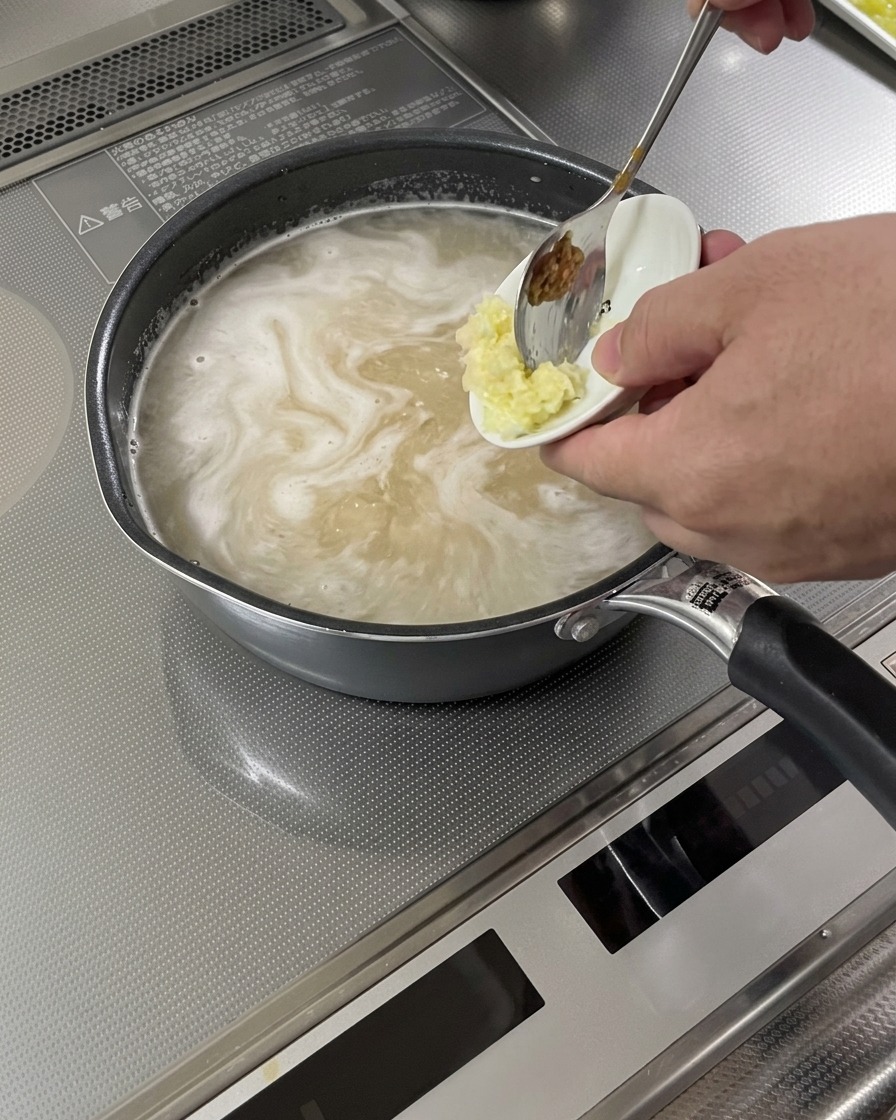 Grated garlic and ginger being added to a simmering soup base.