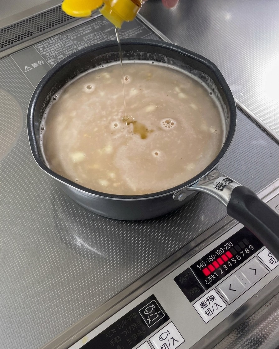 Sesame oil being drizzled into a finished soup base.