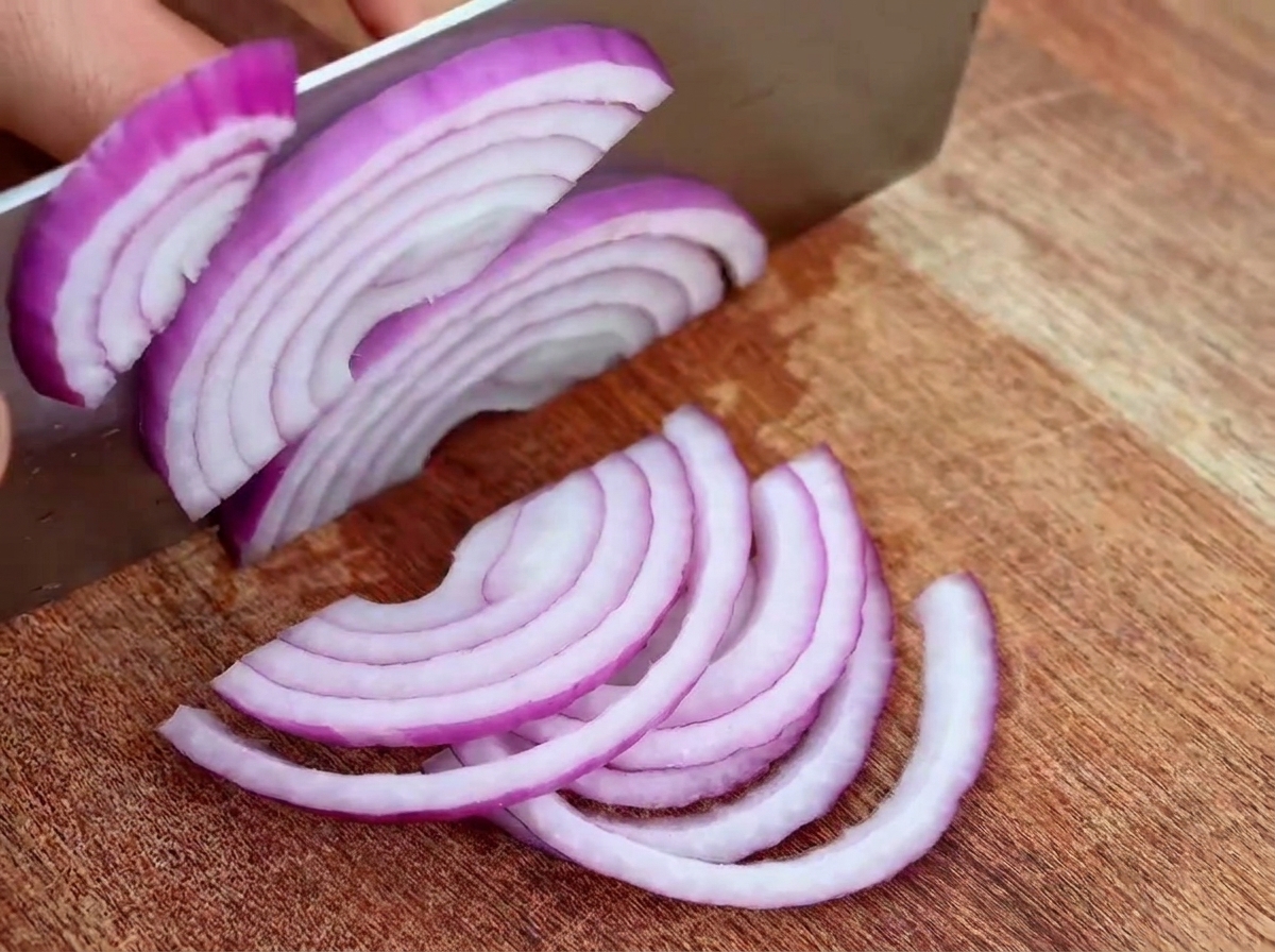 Thinly sliced red onion pieces on a wooden cutting board, ready for the pan.