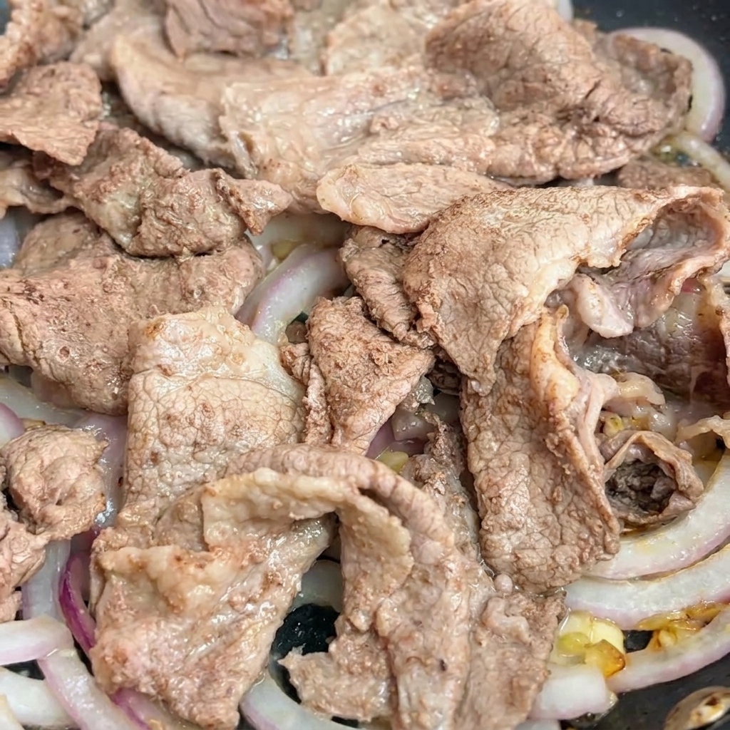 Dark teriyaki sauce being poured into a pan over beef and onion slices.