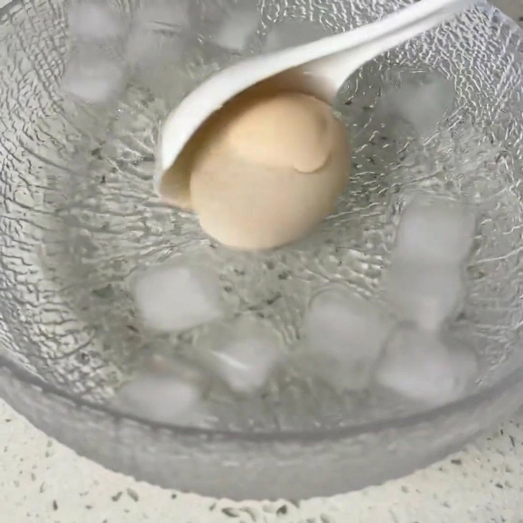 A cooked egg being moved into a glass bowl filled with ice cubes and water.