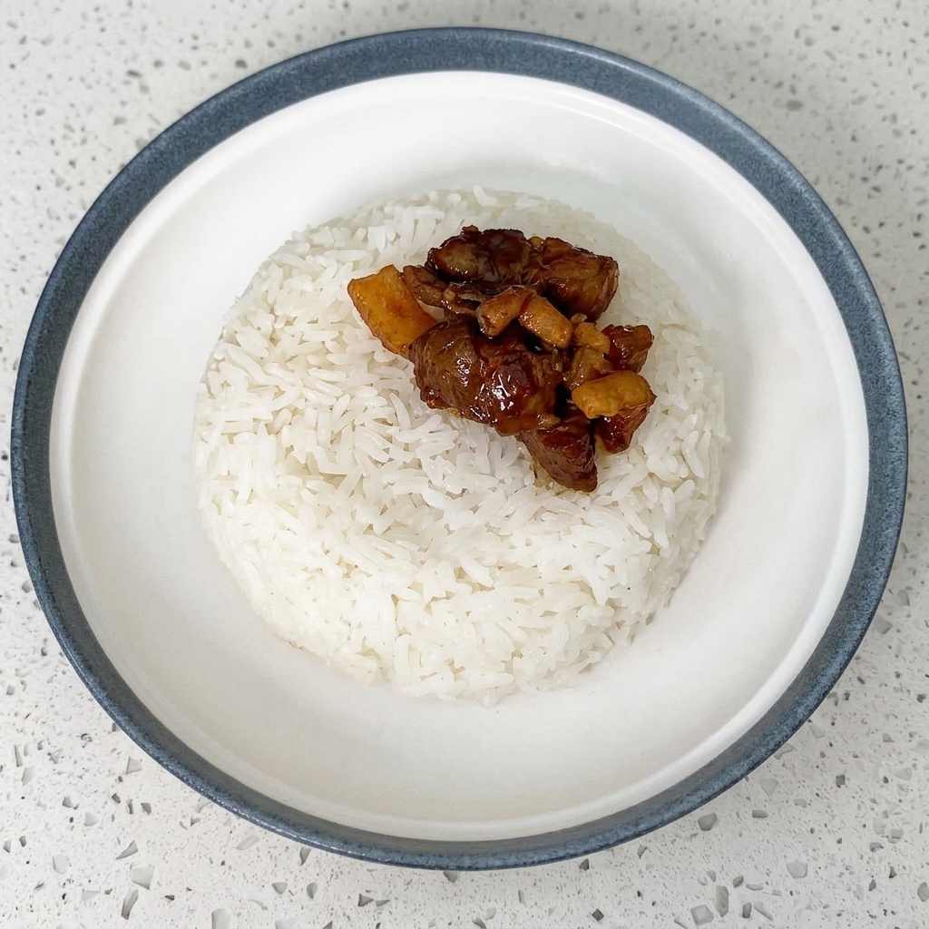 Saucy beef slices being placed with chopsticks onto a bowl of white rice.