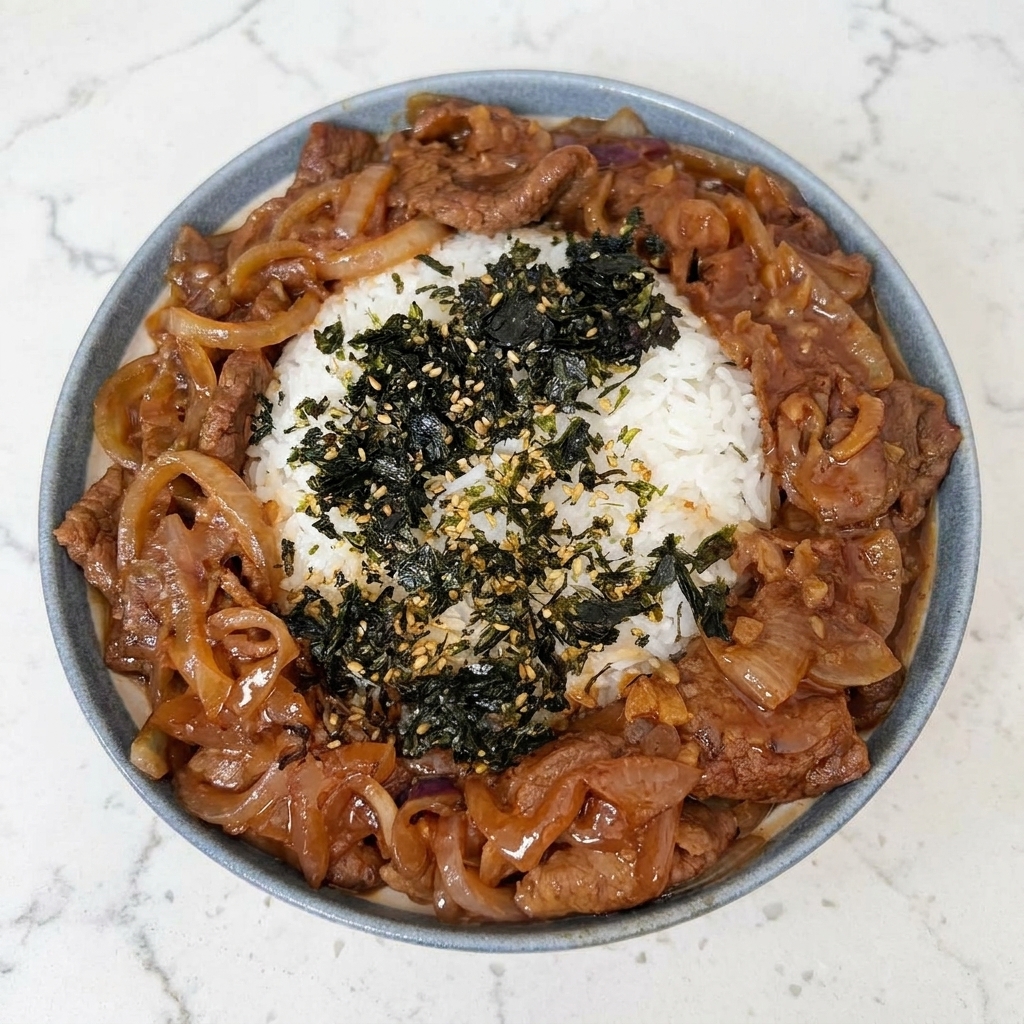 A close-up of a rice bowl being topped with a sprinkle of crushed nori seaweed and toasted sesame seeds.