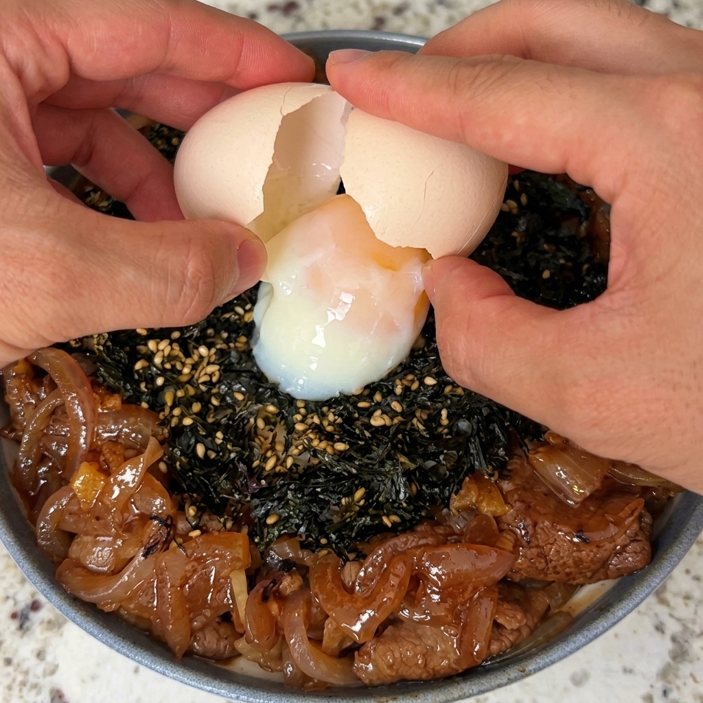 A hot spring egg being carefully cracked open and placed on top of a beef and seaweed rice bowl.