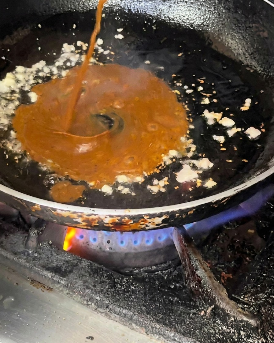Dark sauce being poured into a pan containing sautéed minced garlic and onion.