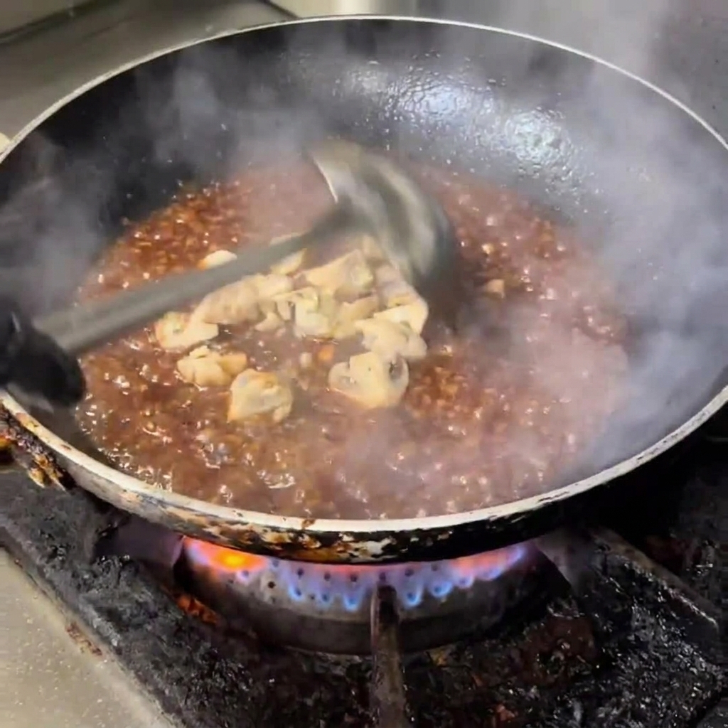 Diced button mushrooms simmering in a glossy, dark, and savory sauce in a frying pan.