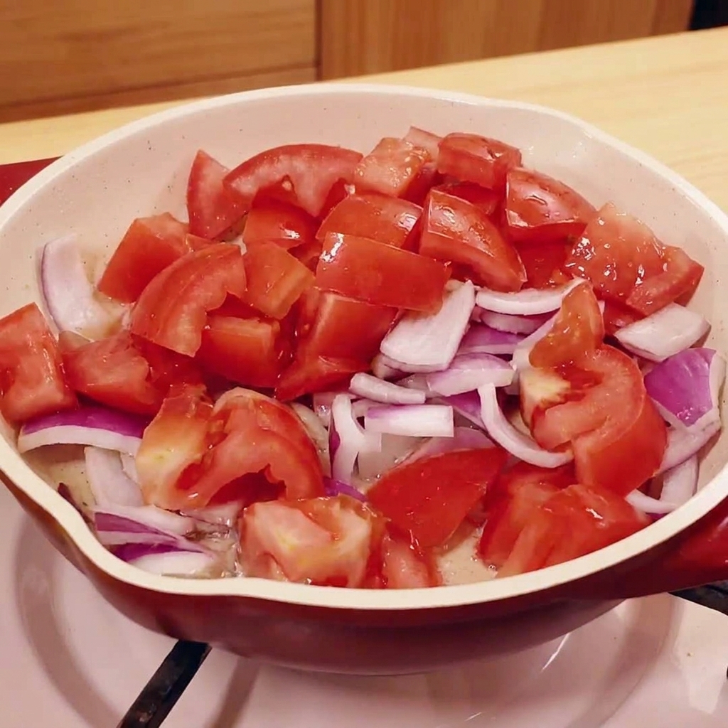 Chopped tomatoes and red onions cooking in a pan.