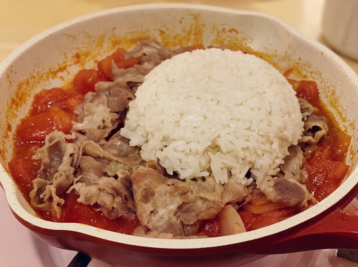 A dome of white rice sitting on top of the beef and tomato mixture in a pan.