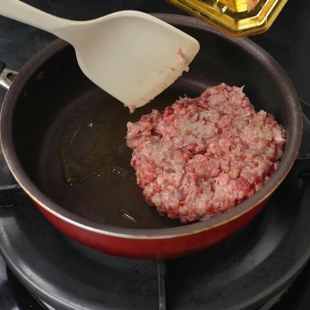 Ground beef being placed into a pan with oil and broken apart with a spatula.