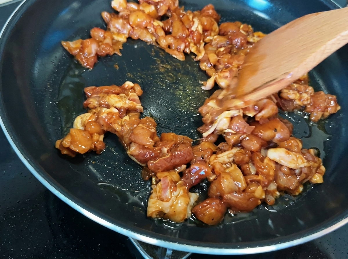 Chicken pieces being stir-fried in a pan, showing golden-brown caramelization.