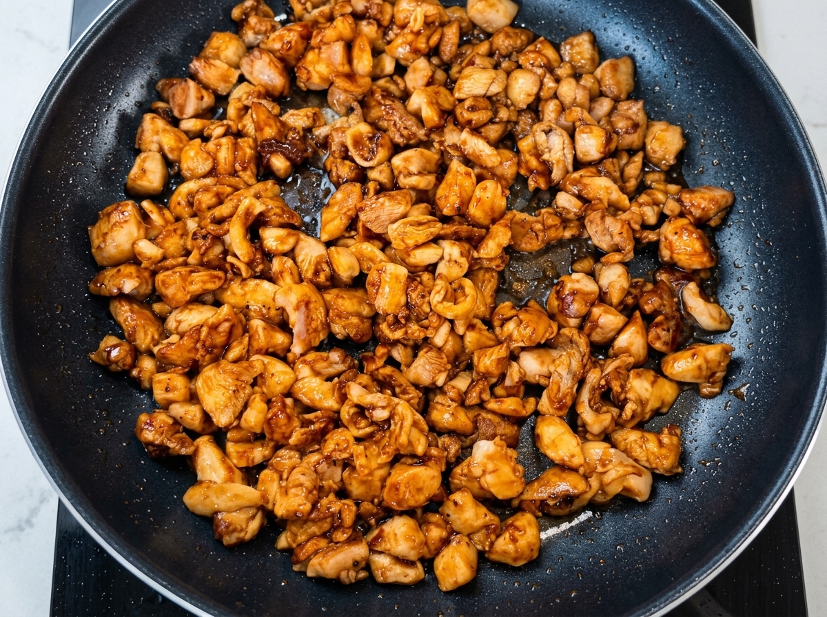 Chopped scallions being tossed into the pan with browned chicken.