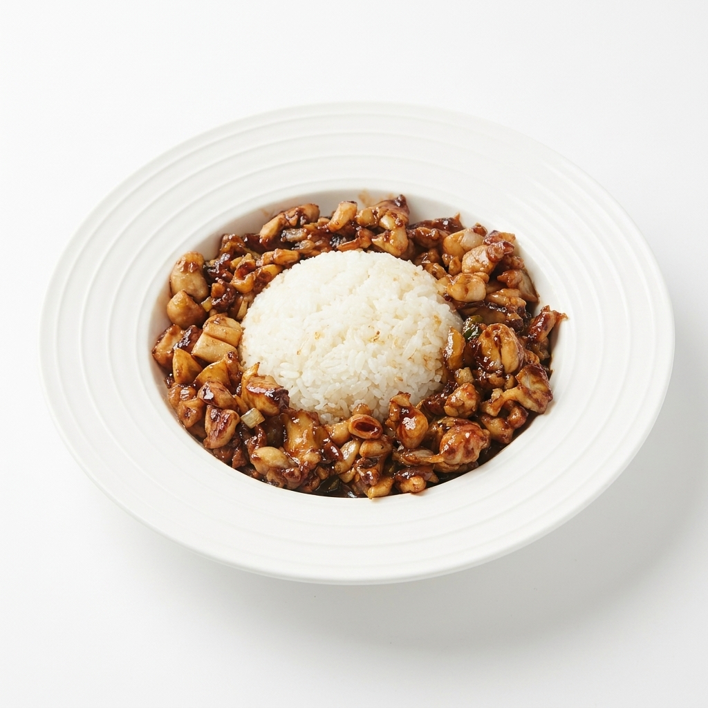 Glazed chicken stir-fry being arranged around the rice mound on a white plate.