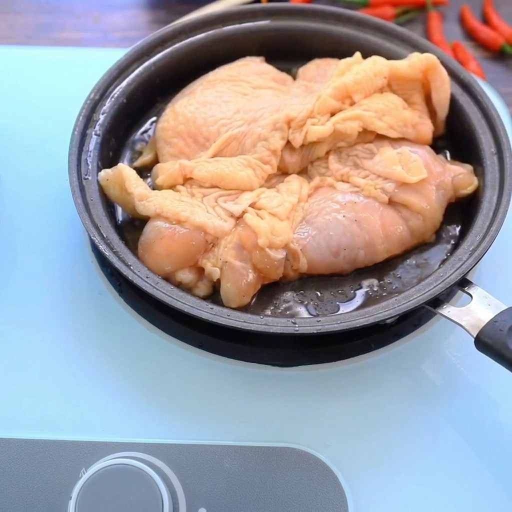 Chicken thighs browning in a hot pan, showing a golden, crispy surface.